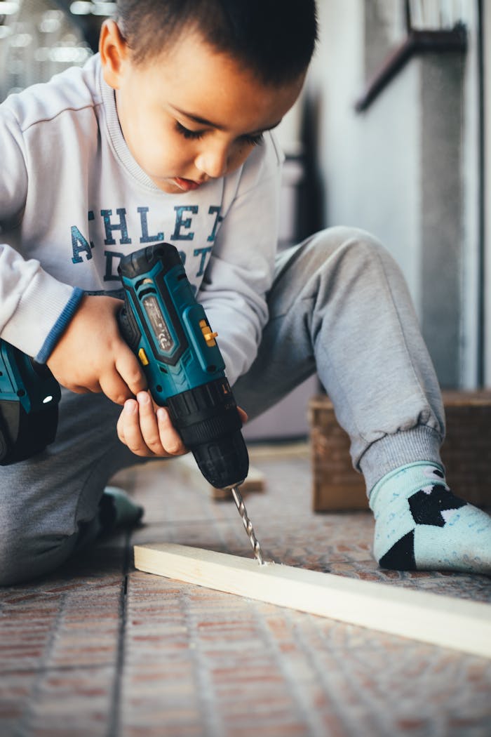 A young boy uses an electric drill on a wooden piece, showcasing early skills development.