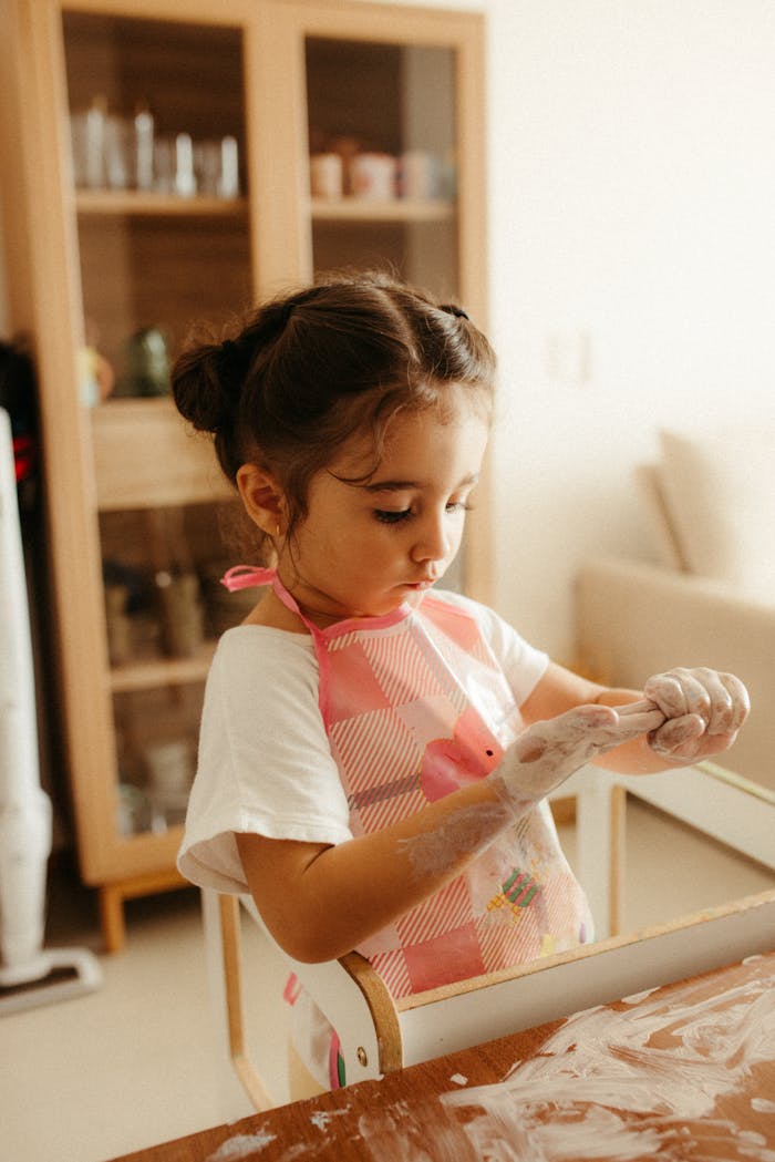 Young child enjoying creative play at home, wearing apron and using play dough.