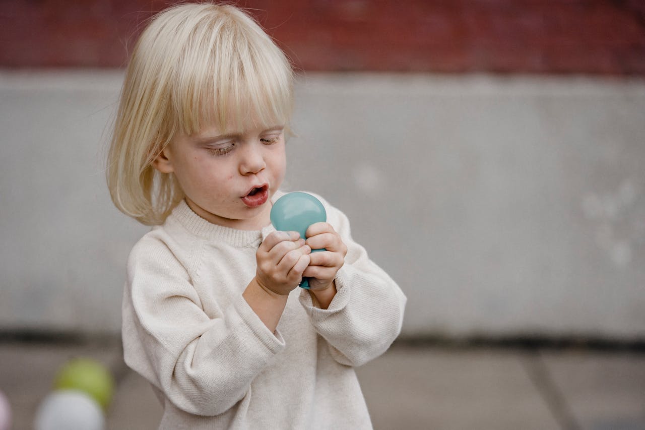 Cute little child in soft wear having fun with small balloon on street pavement in daylight