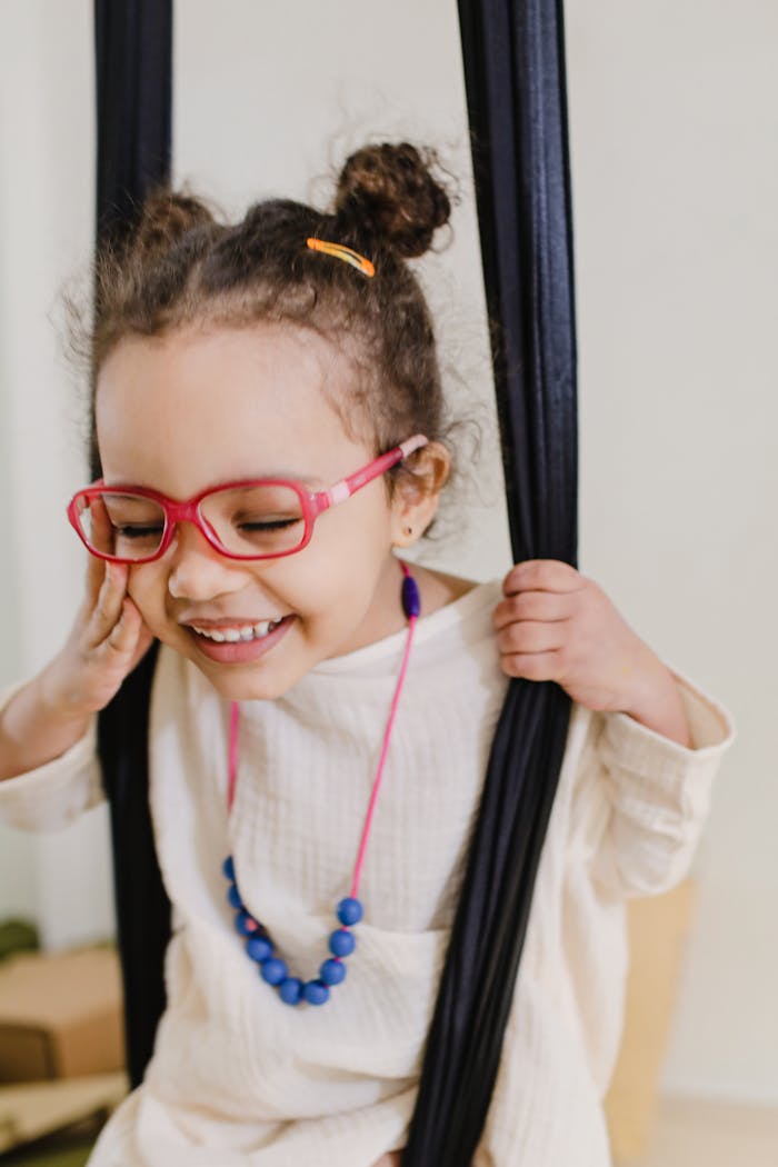 Happy child with red glasses smiling while swinging indoors.